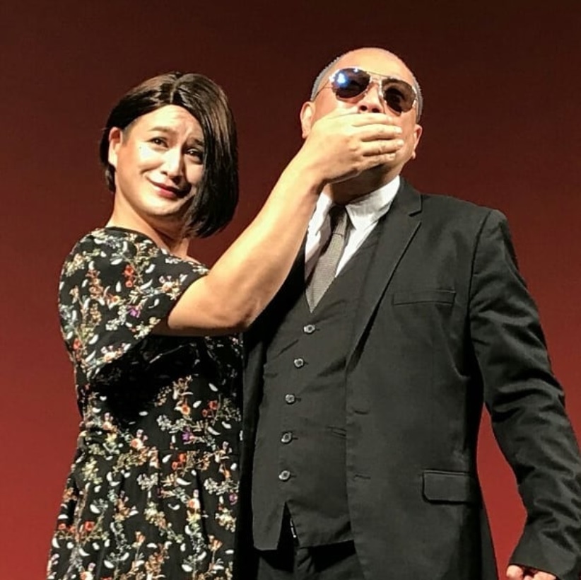 “嫁の代わりに会長の口をふさぐダレノガレ”（画像は『Makoto Izubuchi　2018年8月10日付Instagram「「RGが90分あるあるを歌い続け、ガリットチュウ福島が哀愁モノマネし続ける会」御来場ありがとうございました。」』のスクリーンショット）