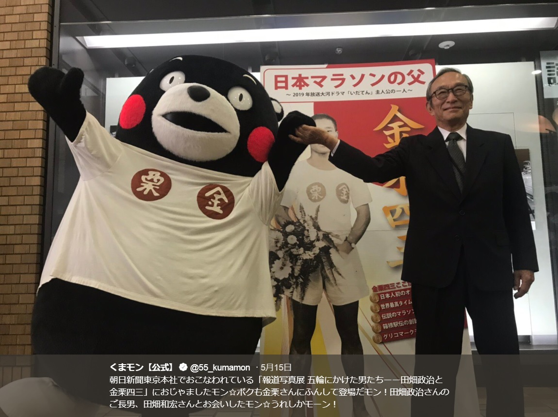 くまモンと田畑政治さんのご長男・田畑和宏さん（画像は『くまモン【公式】　2019年5月15日付Twitter「朝日新聞東京本社でおこなわれている「報道写真展 五輪にかけた男たちーー田畑政治と金栗四三」におじゃましたモン」』のスクリーンショット）