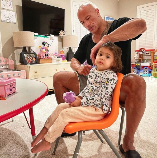 2歳娘の髪をブラッシングするドウェイン・ジョンソン（画像は『therock　2021年1月22日付Instagram「Now despite my two year old looking completely TERRIFIED for her life that daddy is solely responsible for getting all the painful tangles out of her hair...」』のスクリーンショット）