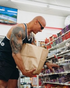 陳列棚にあるチョコレートバーを買い占めるドウェイン（画像は『Dwayne Johnson　2022年11月28日付Instagram「Had to “right the wrong” back home in Hawaii after all these years」』のスクリーンショット）