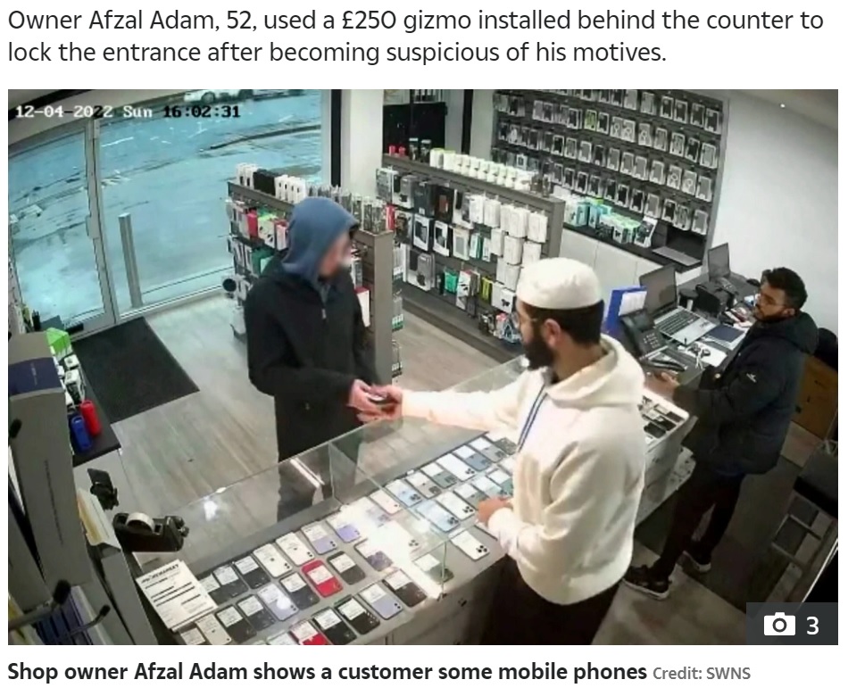 ショーケースの前でスマホを見ていた男（画像は『The Sun　2022年12月6日付「ESCAPE’S CUT OFF Moment bungling thief tries to flee shop with stolen phones ― but can’t open the DOOR」（Credit: SWNS）』のスクリーンショット）