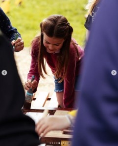 公園のベンチの塗装作業をするシャーロット王女。ペイントブラシを持ちながら、慎重に塗っている様子（画像は『The Prince and Princess of Wales　2023年5月8日付Instagram「＃TheBigHelpOut with The ＠scouts」』のスクリーンショット）