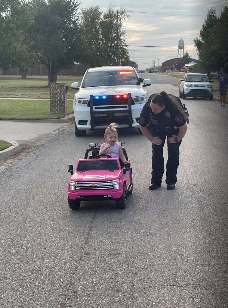 ピンクの車はローズちゃんの2歳の誕生日プレゼントだった。スミス警察署長がカメラを回す中、マネス警察官と話をするローズちゃん。住民皆が顔見知りで、お互いに助け合って暮らしているという（画像は米オクラホマ州オカッシュ警察署長スミス氏提供）